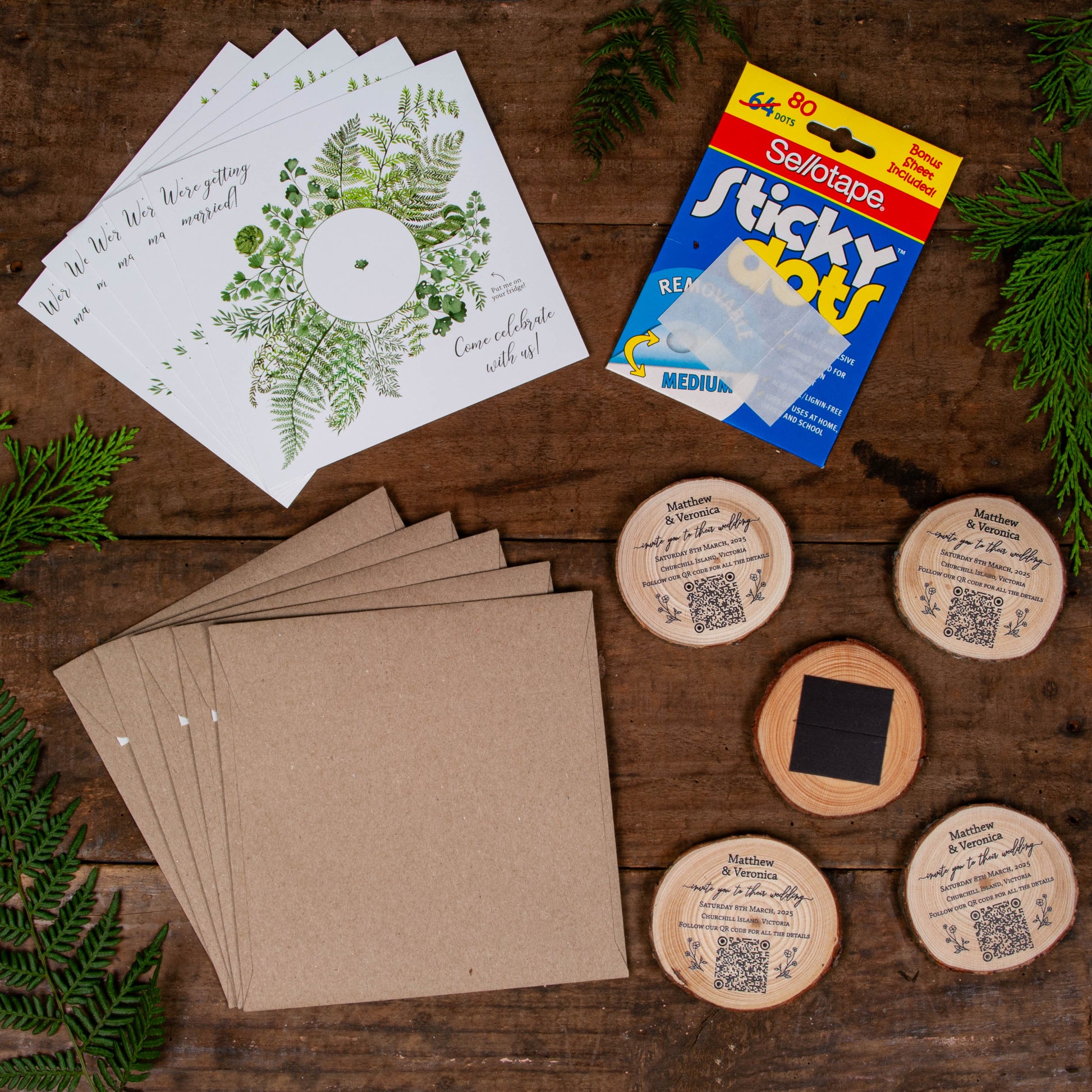 Flatlay of fern card wood slice wedding invitation showing card, envelope, wood slice magnet and sticky dots